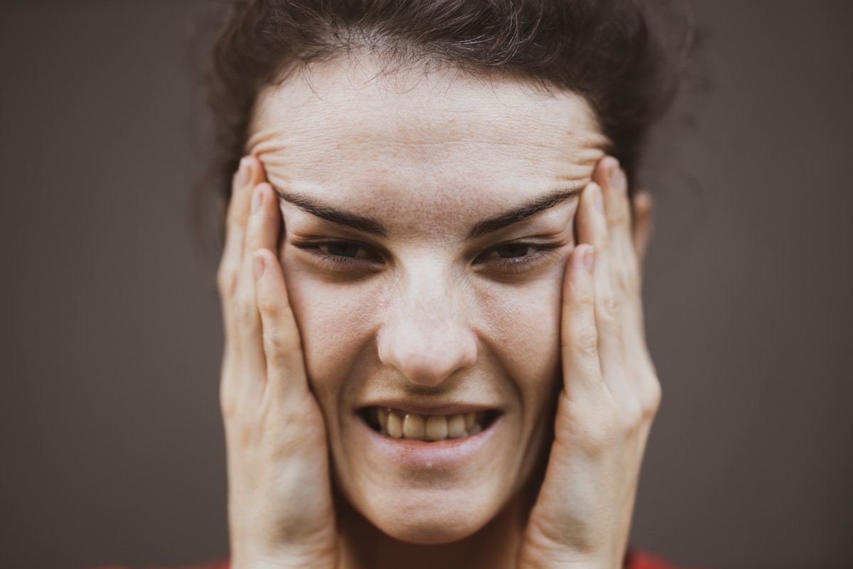 Femme stressée, mains sur le visage, expression de douleur et de frustration.