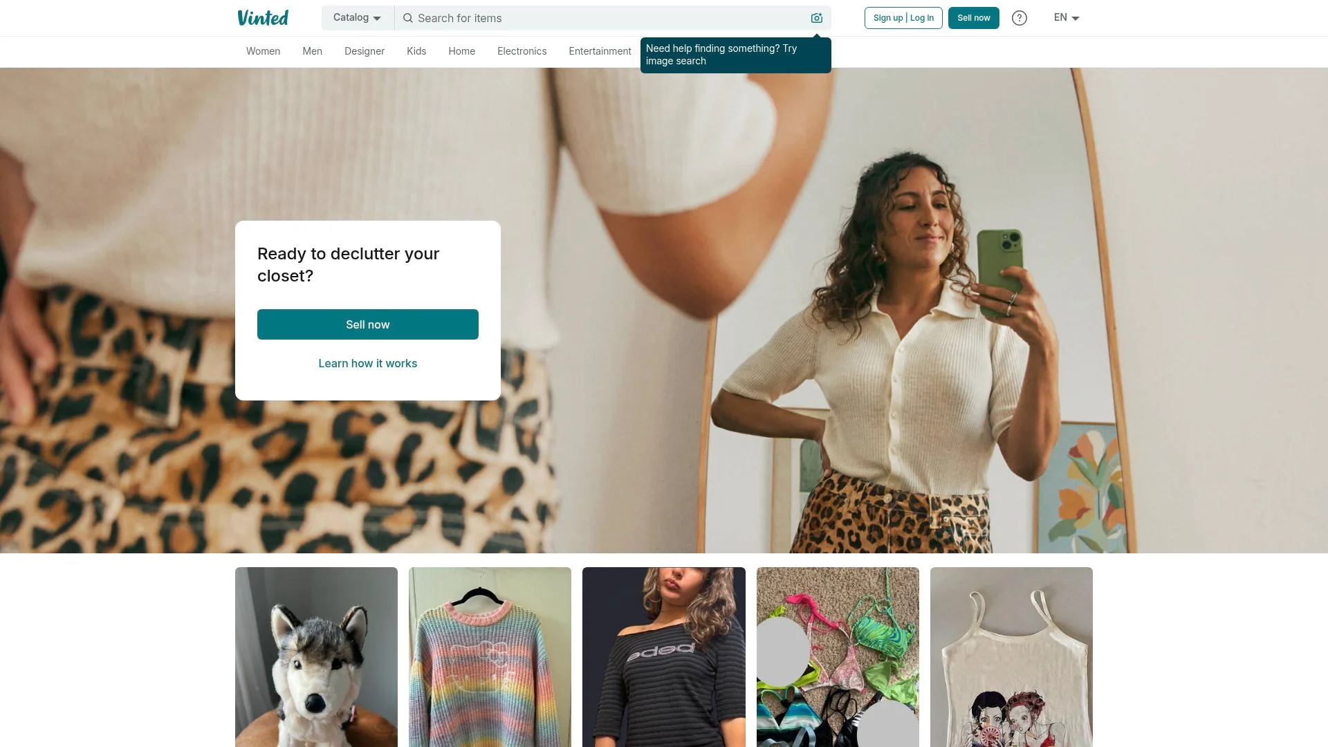 Woman taking a selfie in a room with various clothing items.