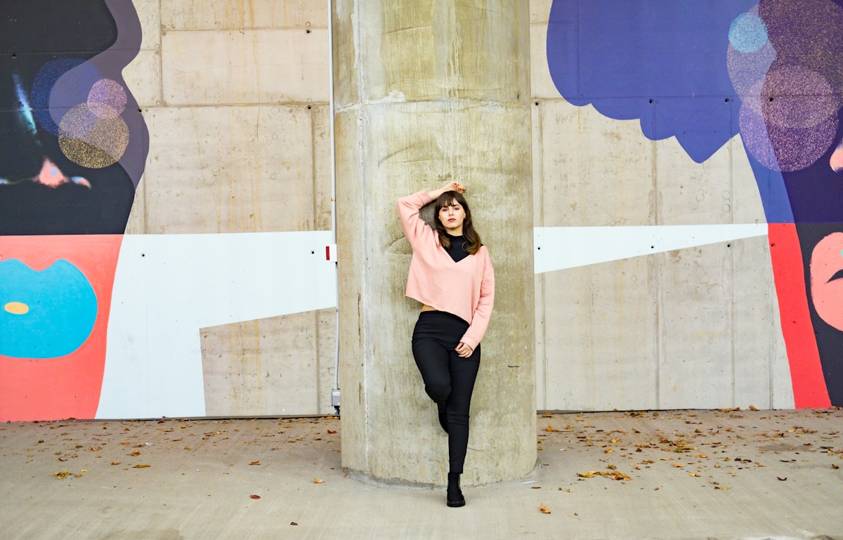 Jeune femme en vêtements roses et noirs devant un mur coloré.
