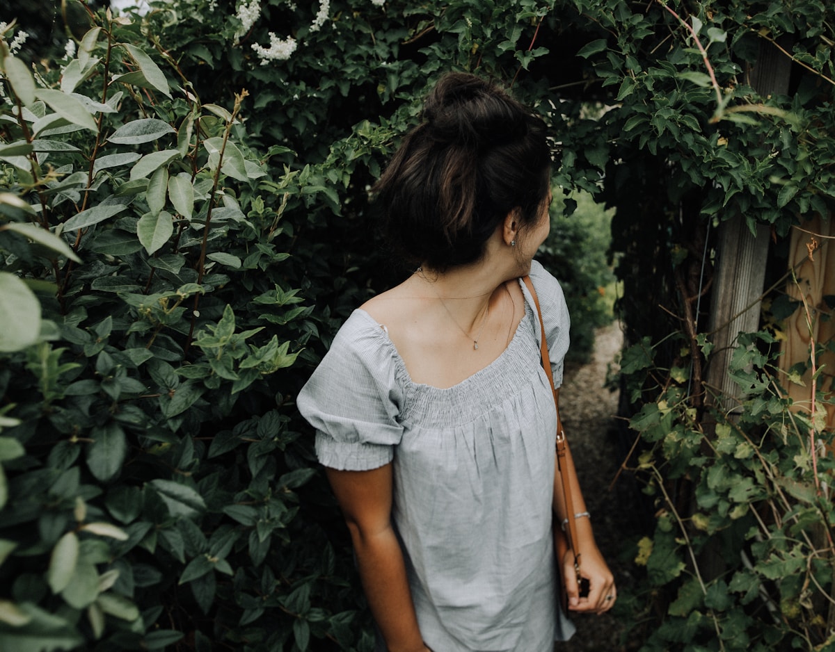 Femme en robe grise dans un jardin verdoyant.