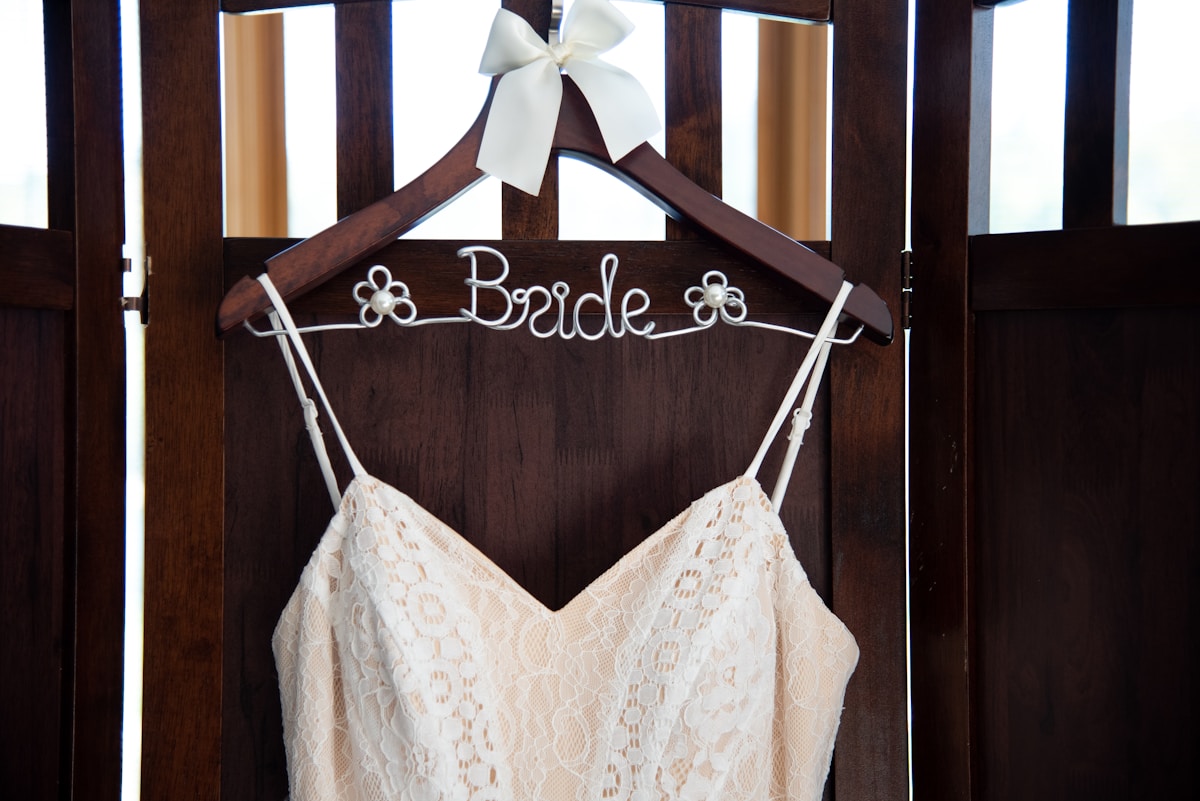 a wedding dress hanging on a wooden hanger