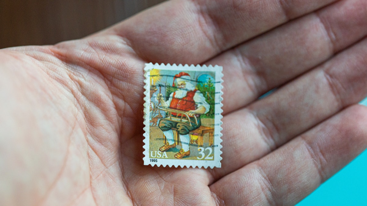 A hand holds a small postage stamp.