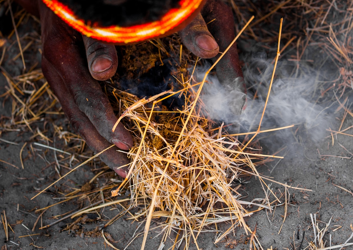 Des mains allumant un feu avec de l'herbe sèche.