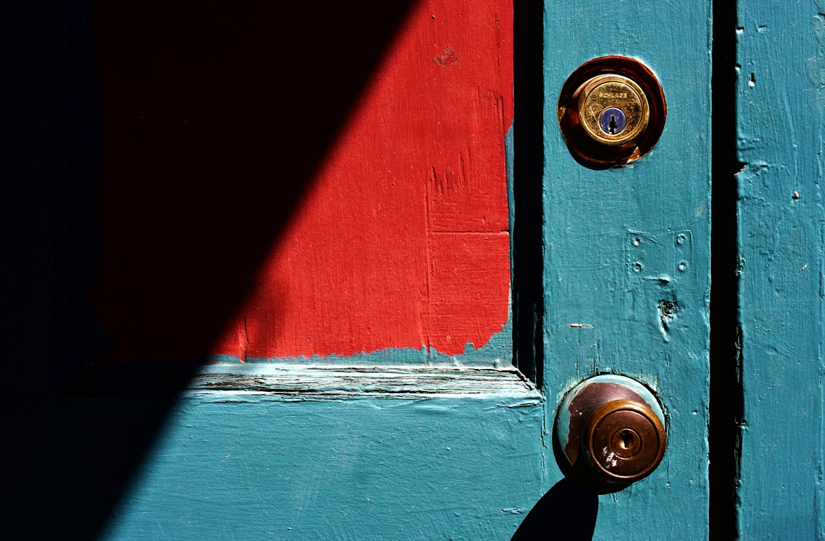 Porte turquoise et rouge avec deux serrures dorées.