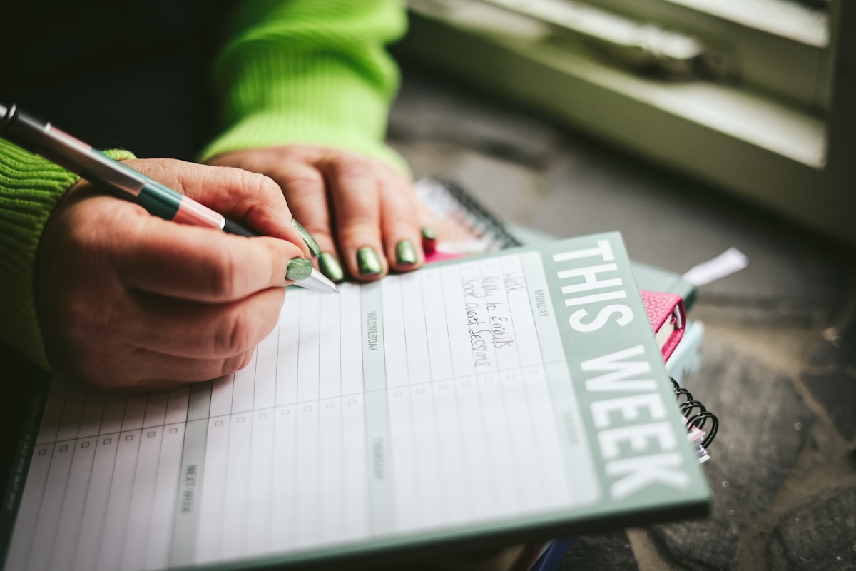 Mains écrivant dans un cahier avec le texte "This week".