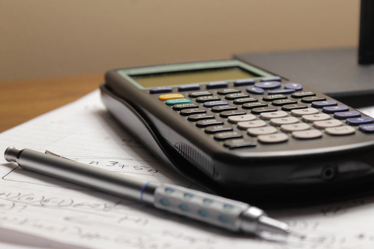 Calculatrice, stylo et feuilles de calcul sur un bureau.
