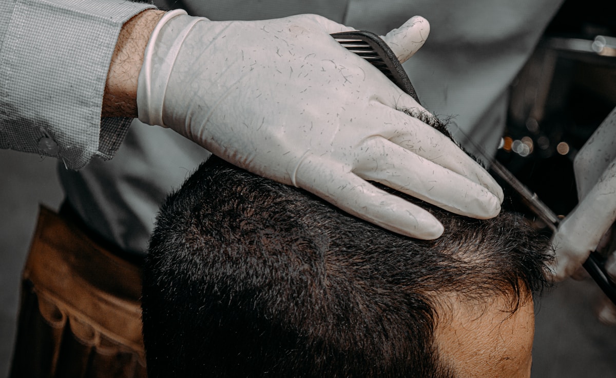 Gros plan sur une main gantée coiffant les cheveux d'un homme.