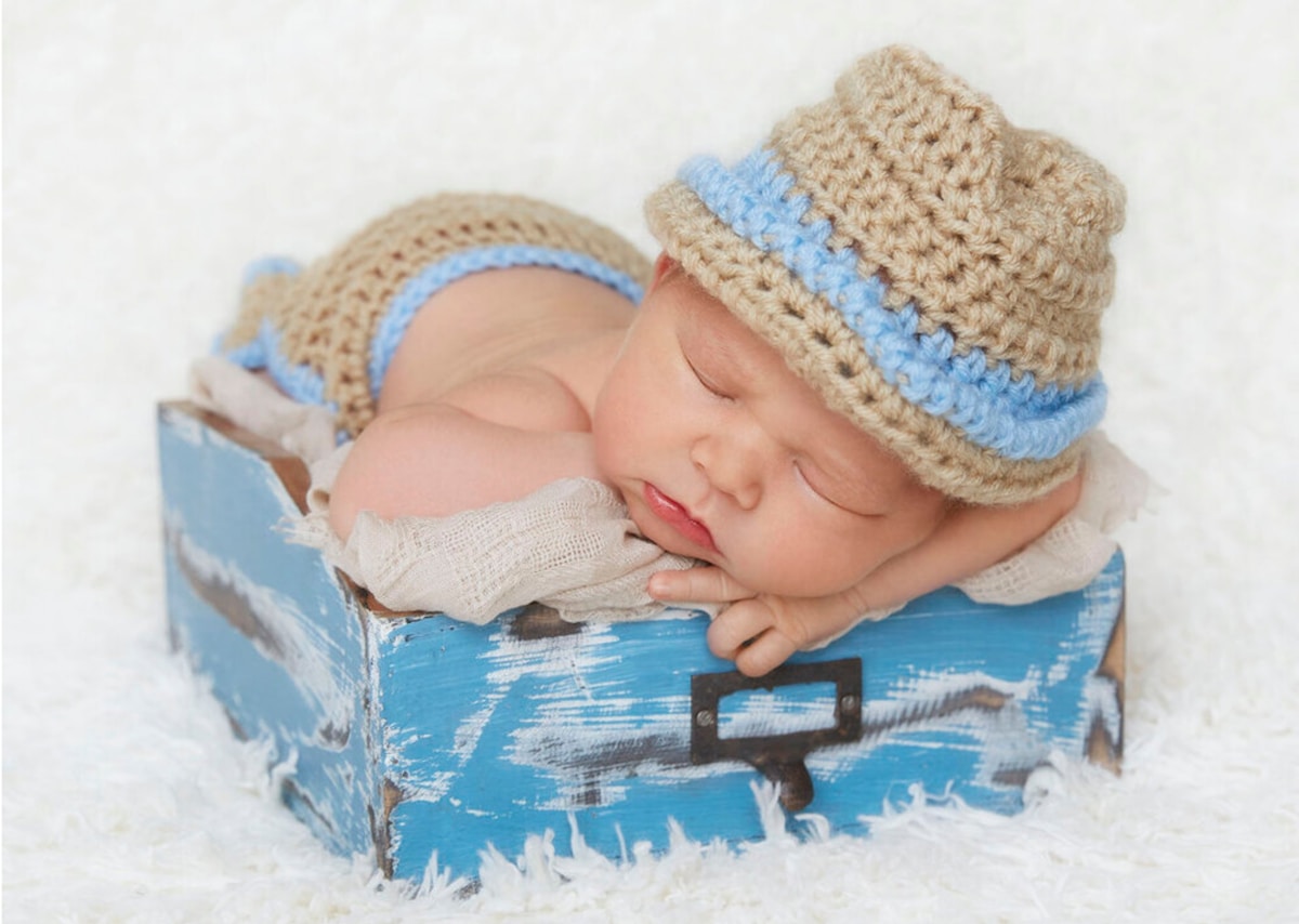 Bébé endormi dans un panier bleu, portant un chapeau en tricot beige et bleu.