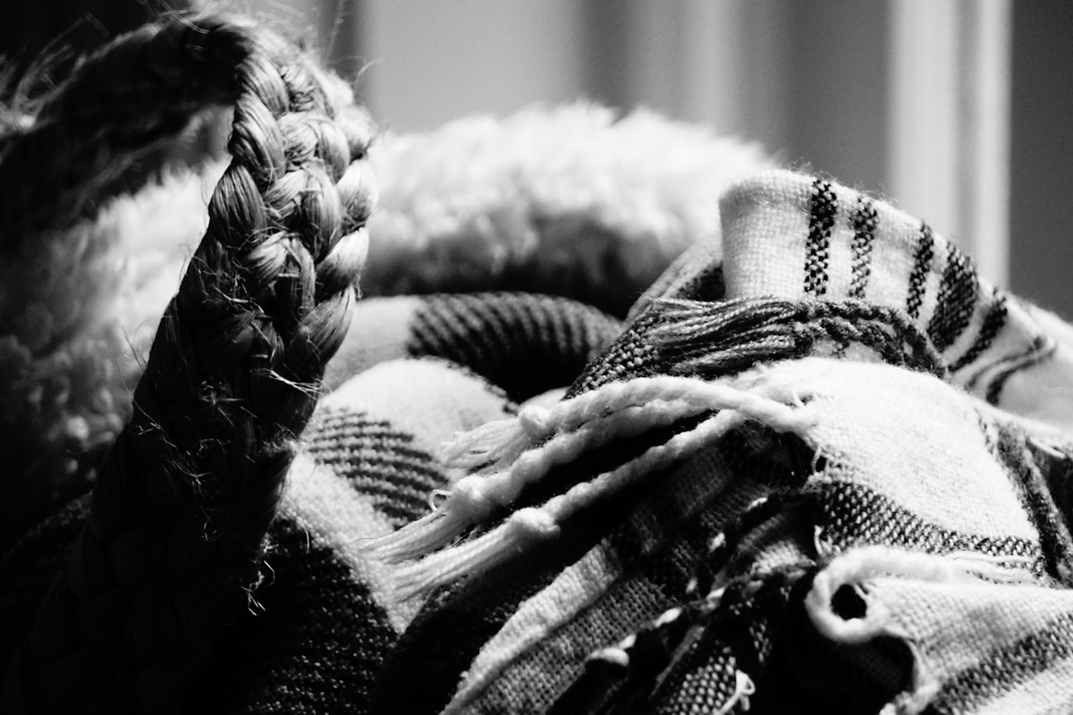 Tresse emmêlée, vêtements chauds et texturés, atmosphère sombre et monochromatique.