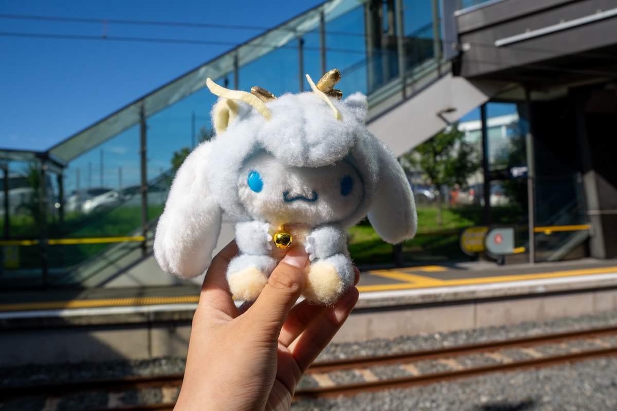 Peluche blanche de créature fantastique avec des yeux bleus et une clochette dorée.