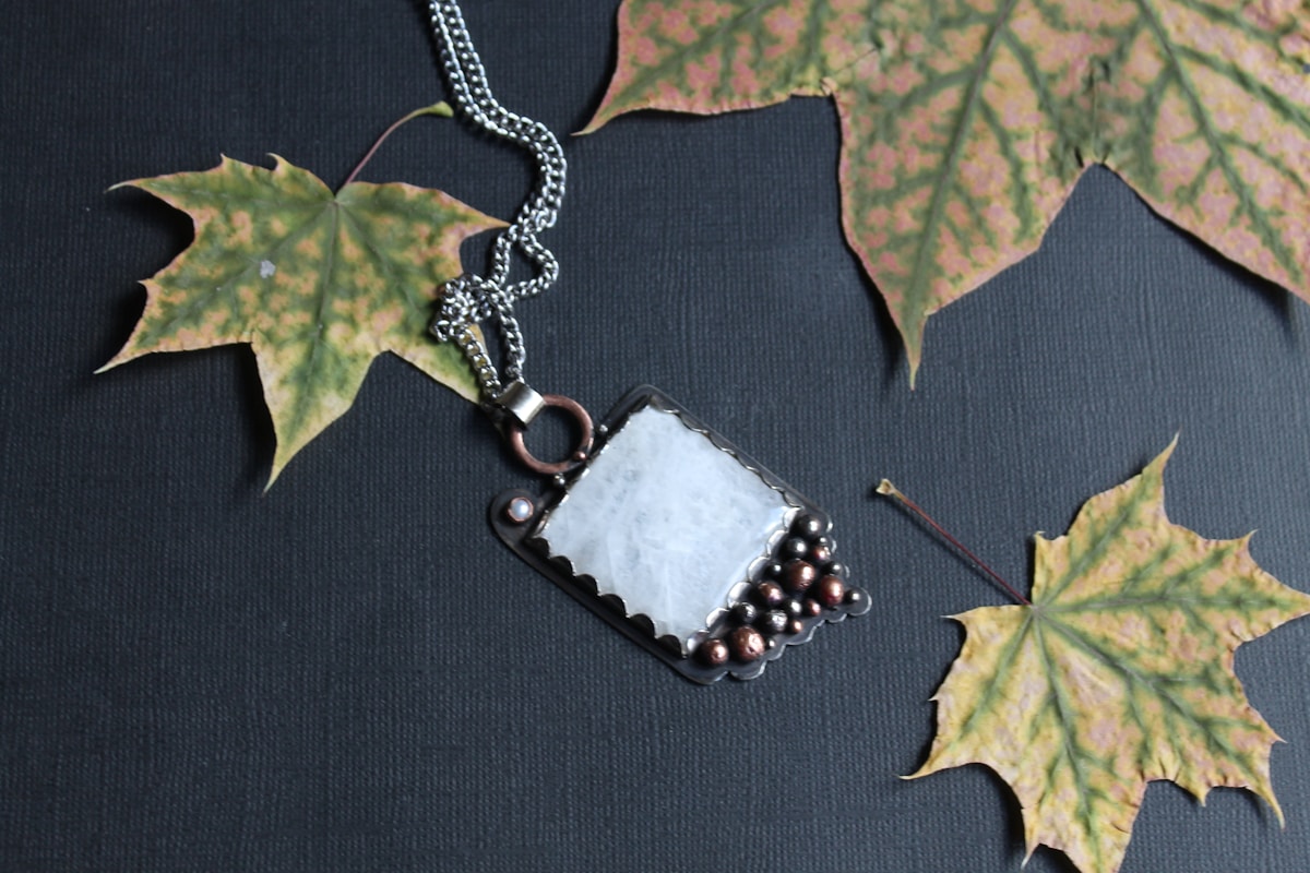 Pendentif en pierre blanche et perles de couleur sur fond noir avec feuilles d'érable.