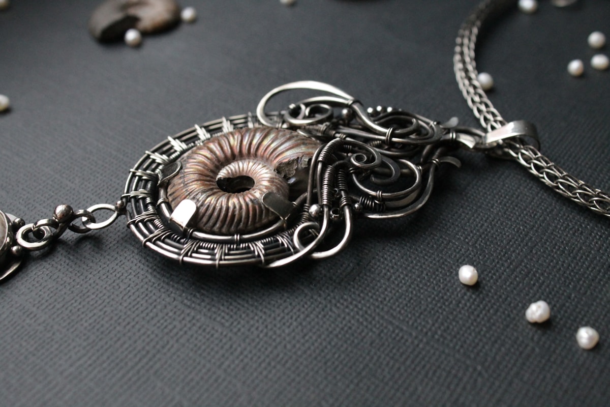 Pendentif en métal noir orné d'un motif spiralé et de perles.