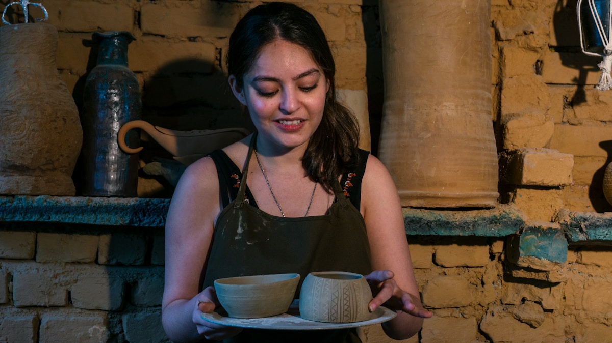 Femme souriante tenant un plateau avec des bols en céramique.