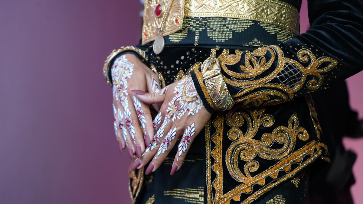 Mains ornées de motifs floraux, vêtements richement décorés de broderies dorées.