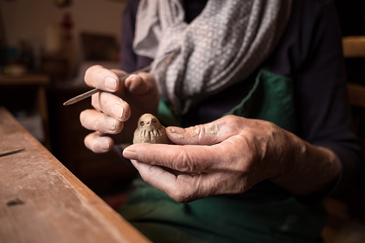 Mains d'un artisan sculptant une figurine en argile.