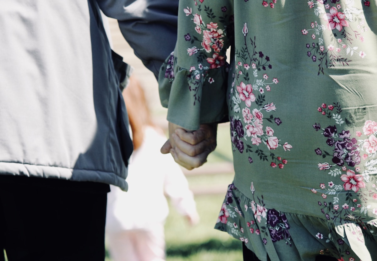 Couple main dans la main, robe fleurie verte et veste noire.