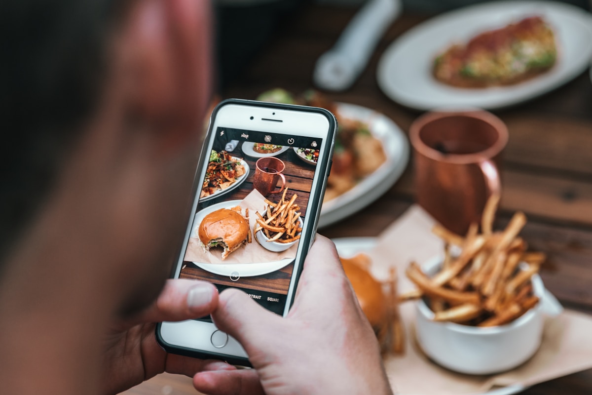 Hamburger, frites et boisson sur une table, photographiés avec un smartphone.