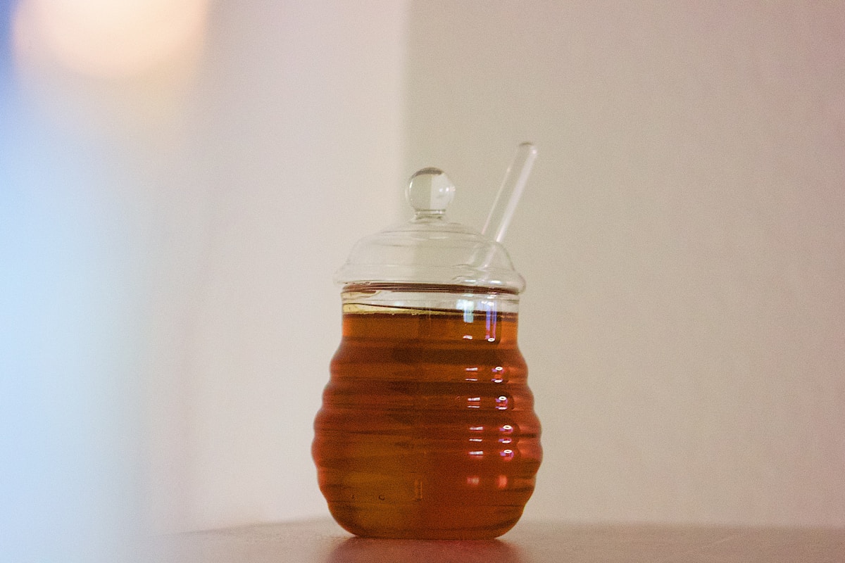 Pot en verre rempli de miel doré avec une cuillère.