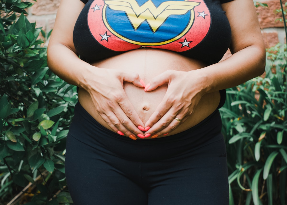 Femme enceinte portant un t-shirt Wonder Woman, mains sur le ventre.