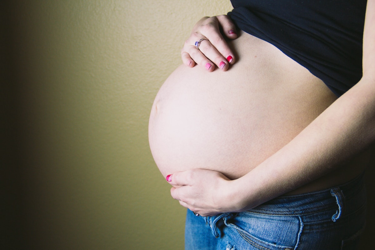Femme enceinte, mains sur le ventre, ongles vernis de rouge.