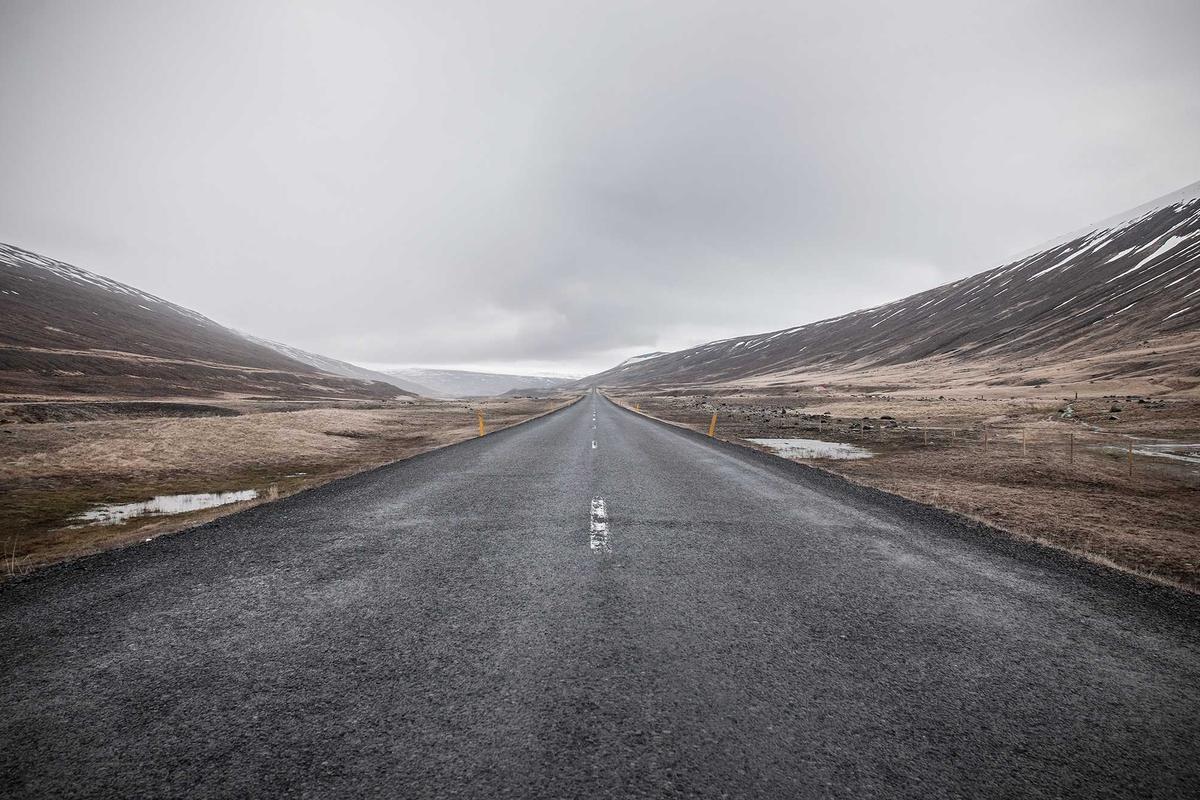 Vast, desolate road stretching through barren, snow-capped mountains.