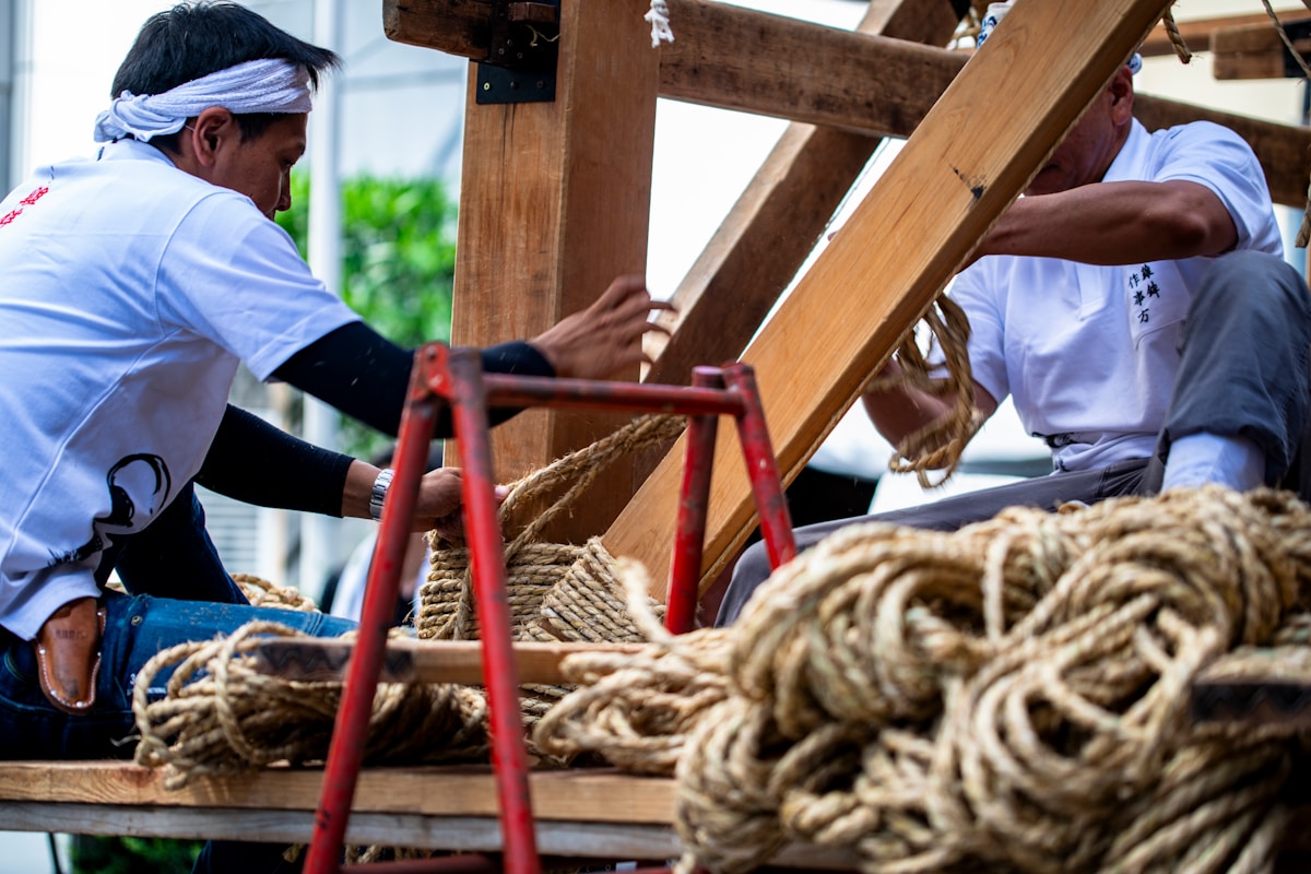 Deux hommes en tenue traditionnelle assemblent une structure en bois avec des cordes.