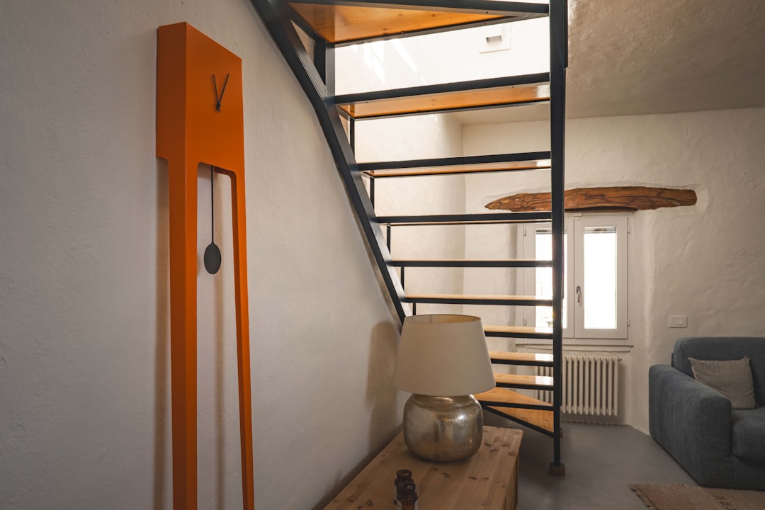 escalier suspendu acier contemporain - A staircase leads up, near an orange clock.