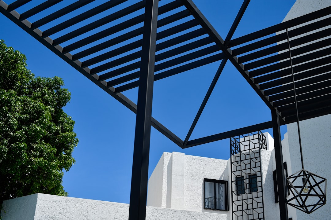 charpente métallique pour villa - Modern black pergola structure against a clear blue sky.