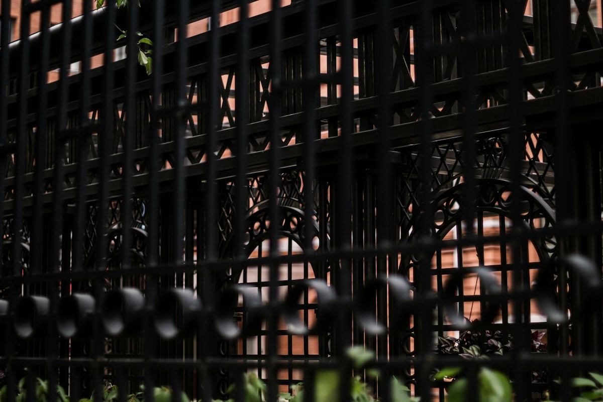 Grille noire ornée devant façade de briques rouges sépia