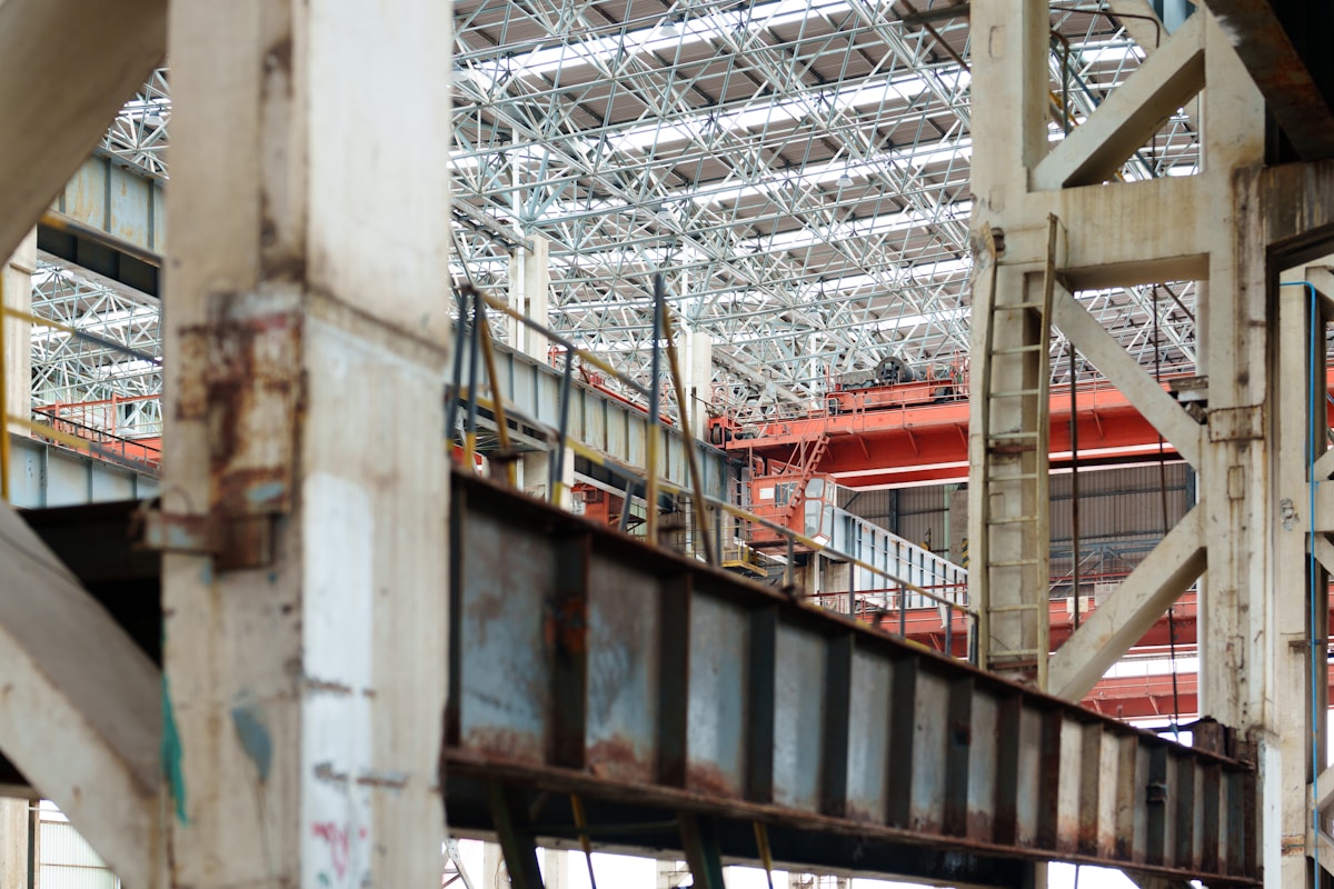 Vaste hangar industriel avec structure métallique et grues rouges.