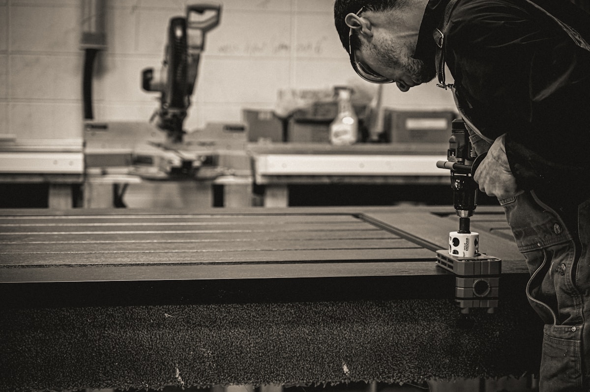 Homme travaillant avec un outil électrique sur un plan de travail en bois.