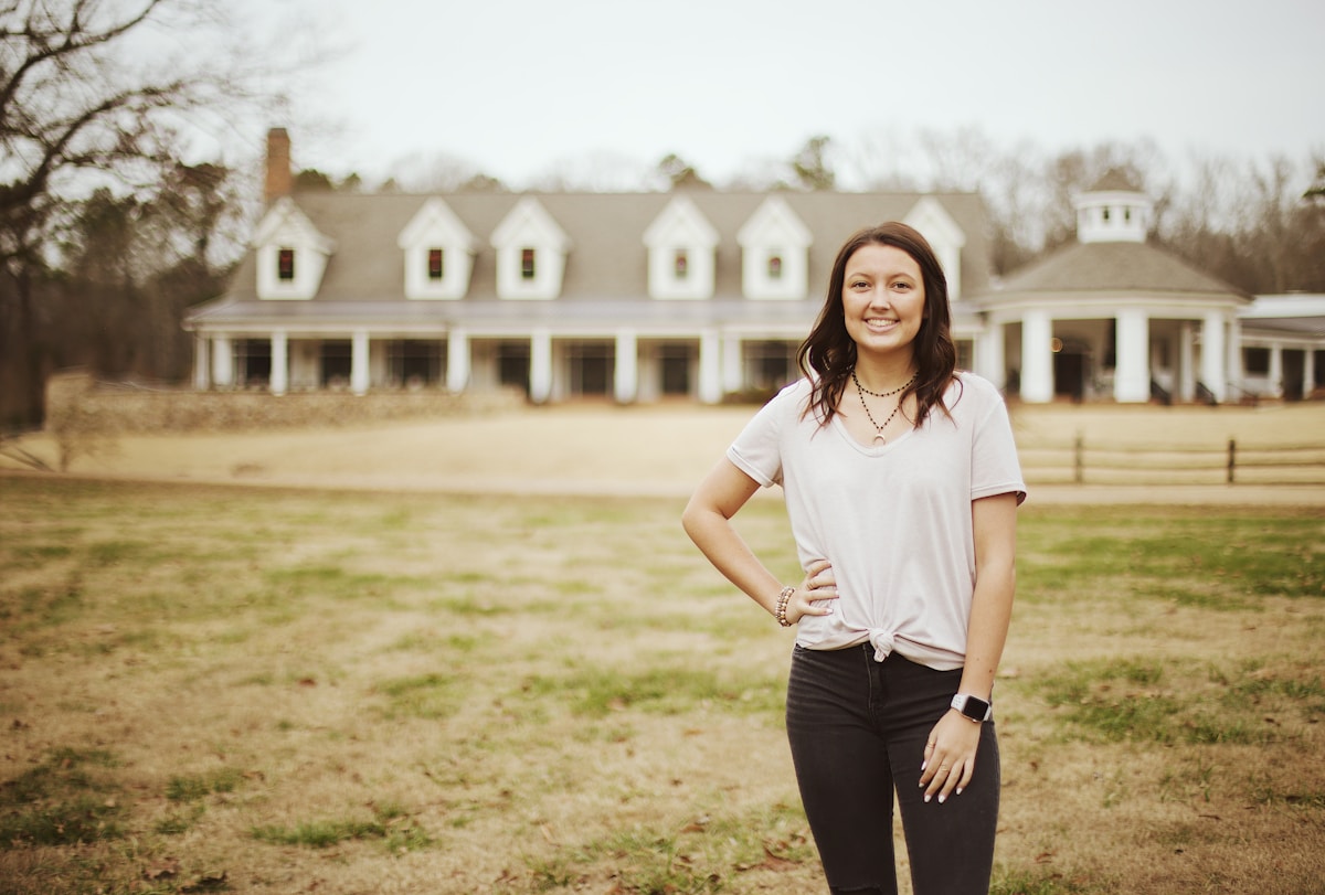 Jeune femme souriante devant une maison de style colonial.