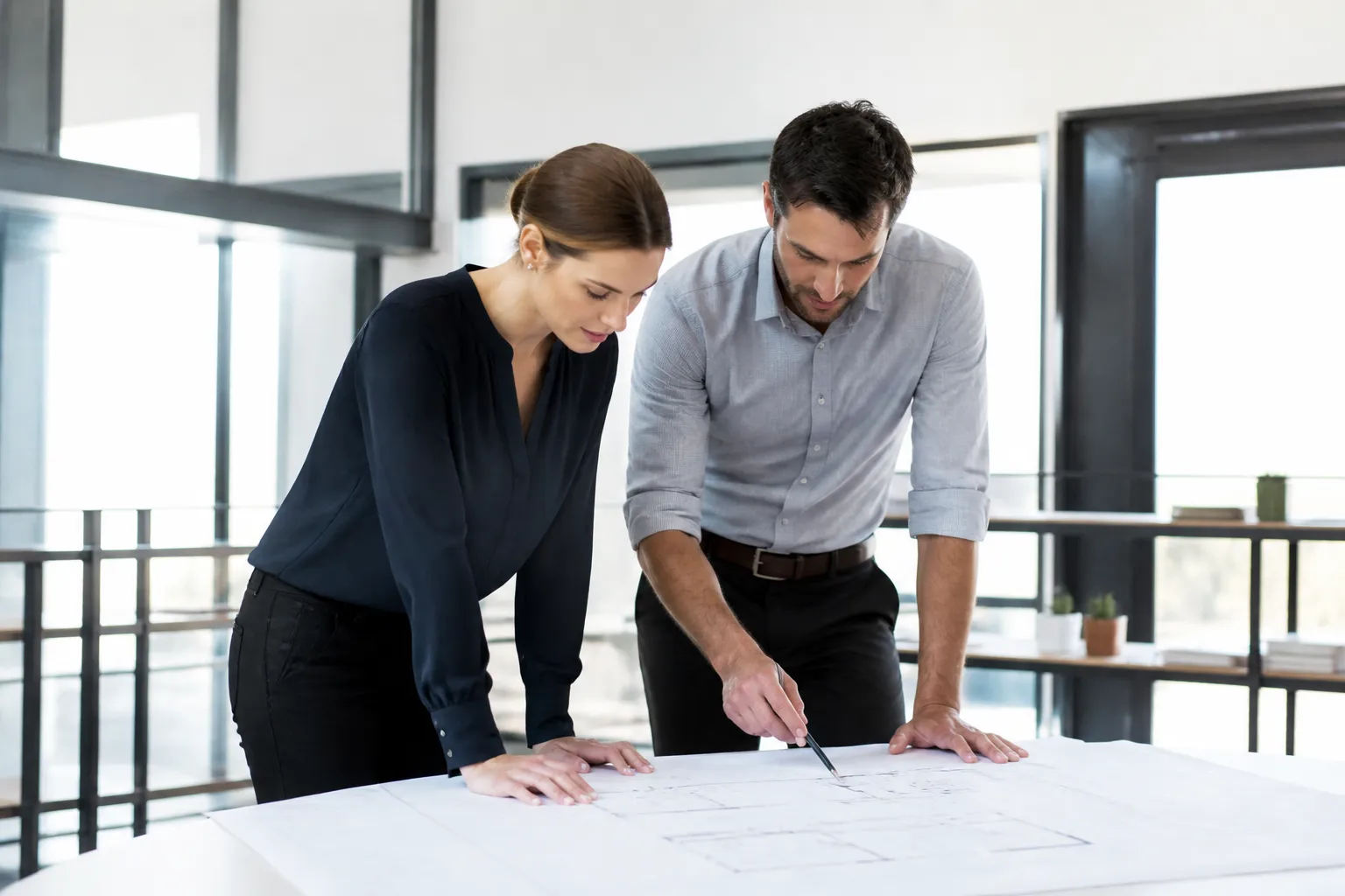 Deux professionnels examinent attentivement des plans sur une table de réunion.