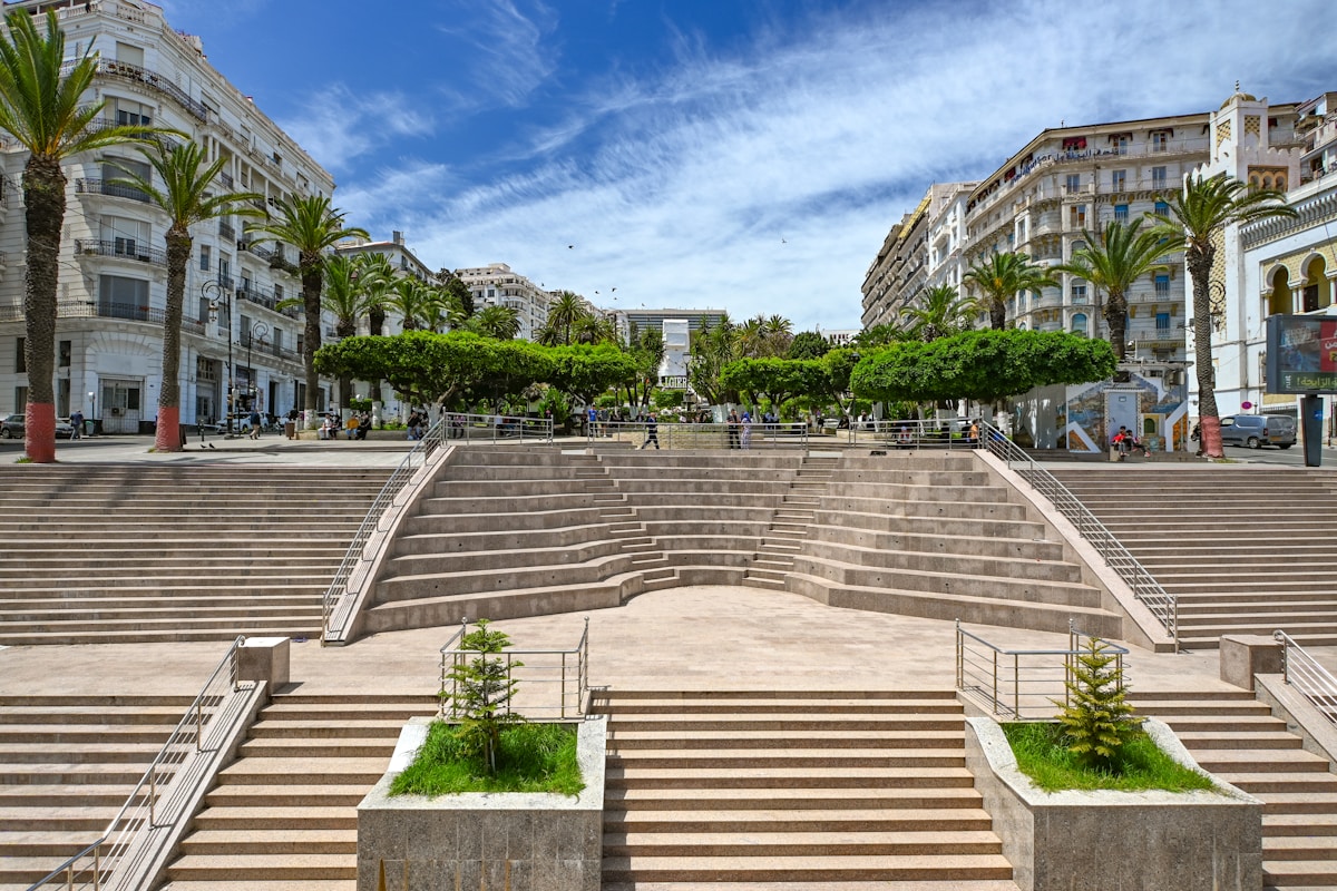 Place publique avec escaliers, palmiers et bâtiments.