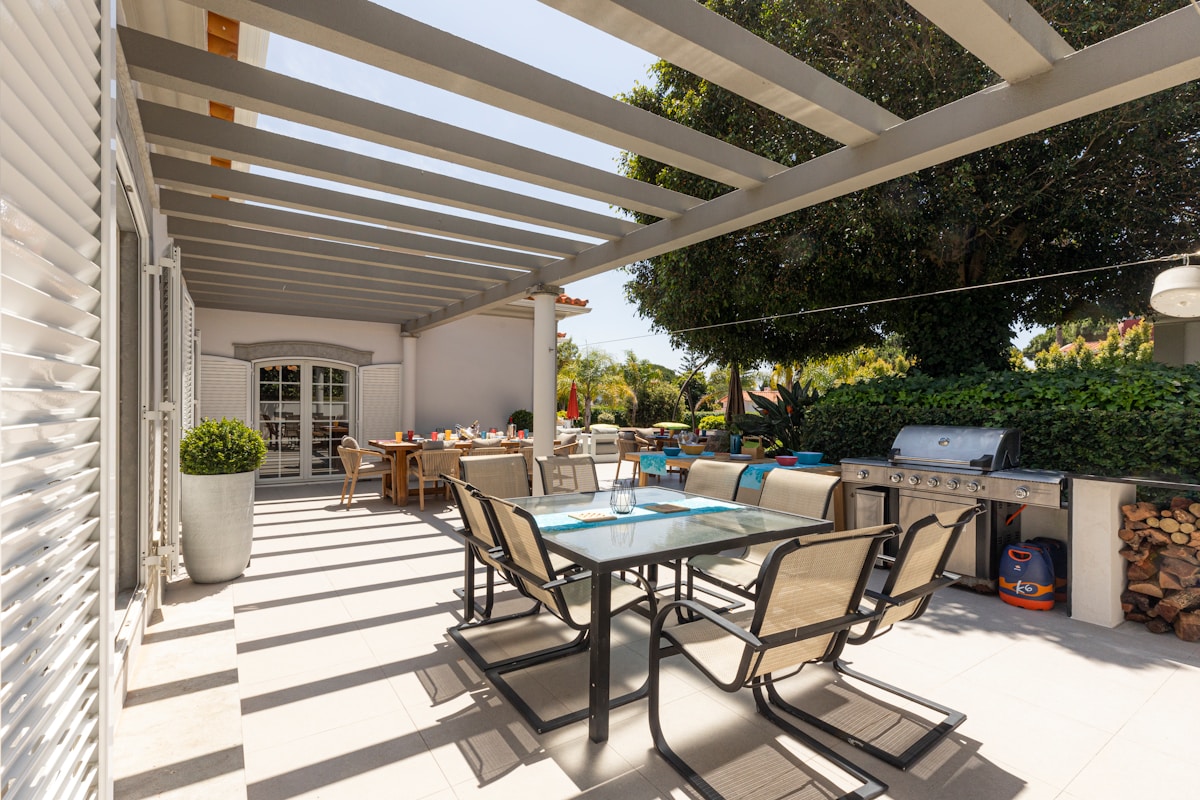 Terrasse couverte avec mobilier de jardin et barbecue.