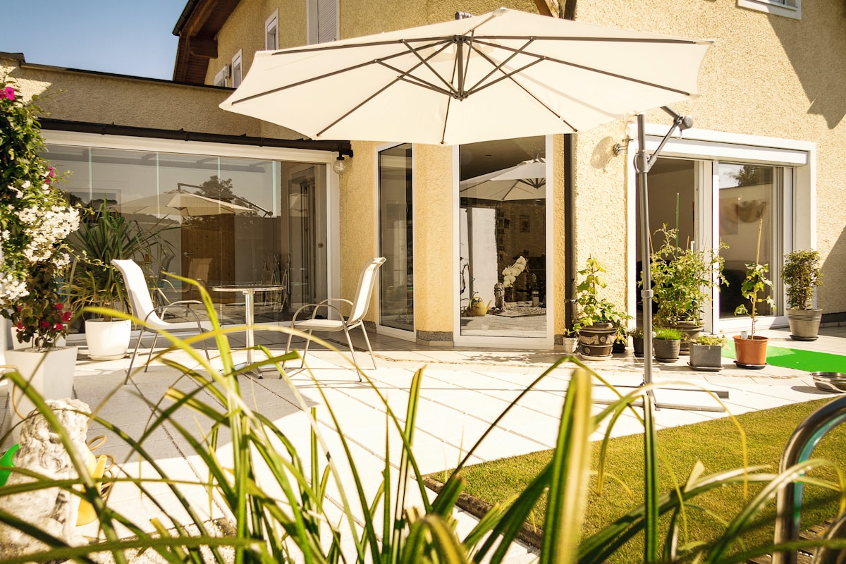 Terrasse ensoleillée avec mobilier de jardin, parasol et plantes en pot.