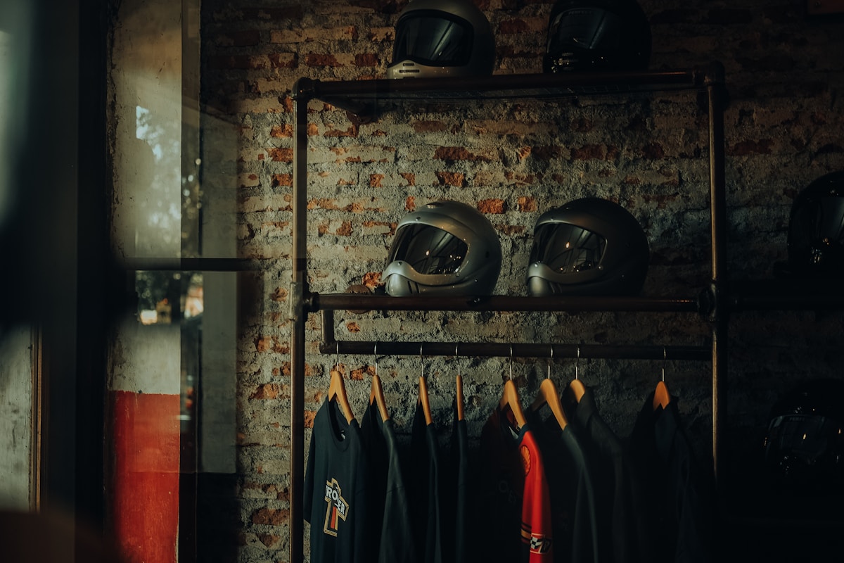 Casques de moto et vêtements suspendus sur une étagère en métal.