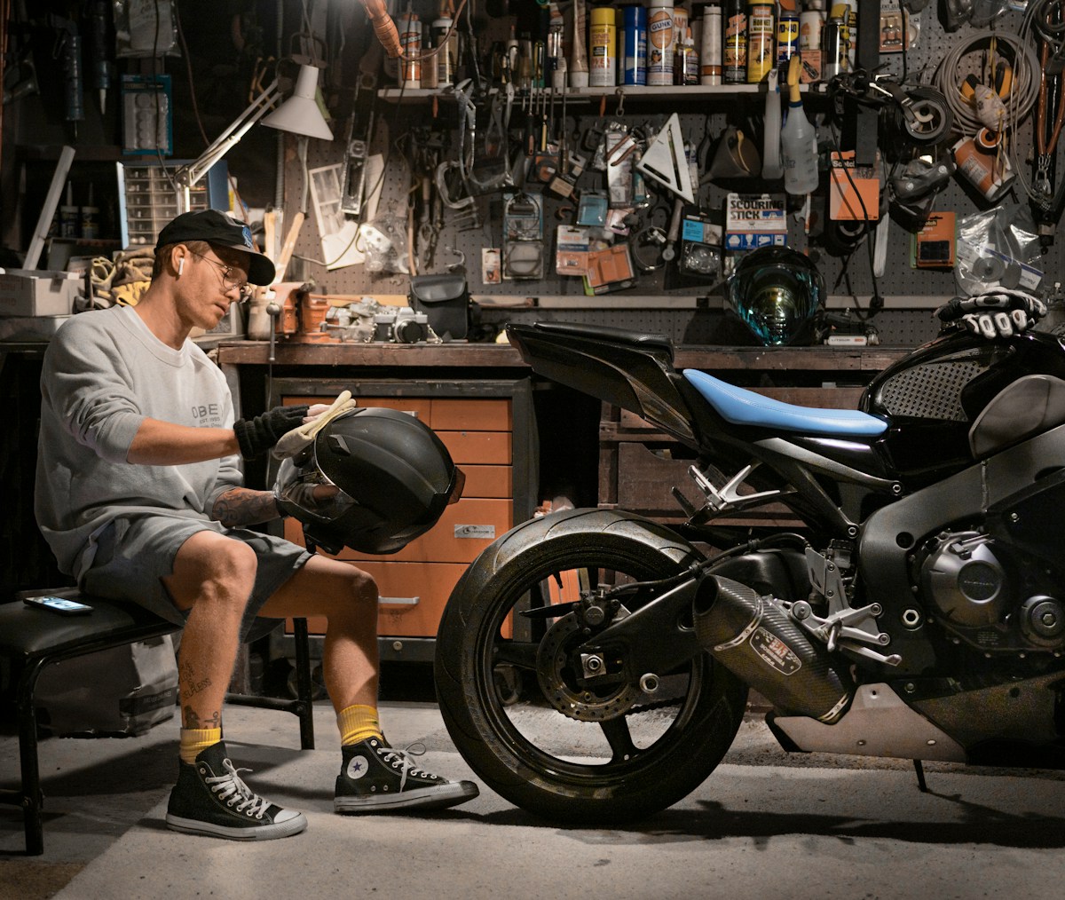 Motard nettoyant un casque près d’une moto noire.
