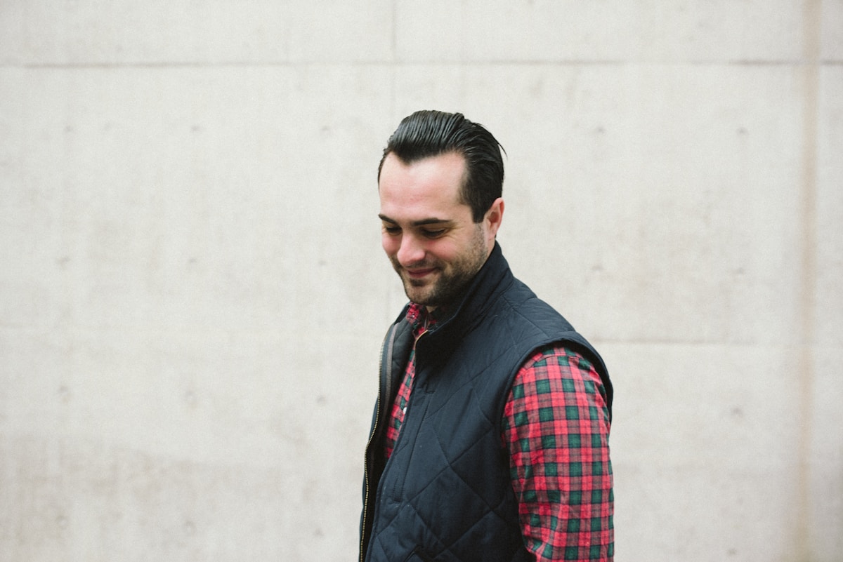 Homme souriant en veste sans manches et chemise à carreaux.