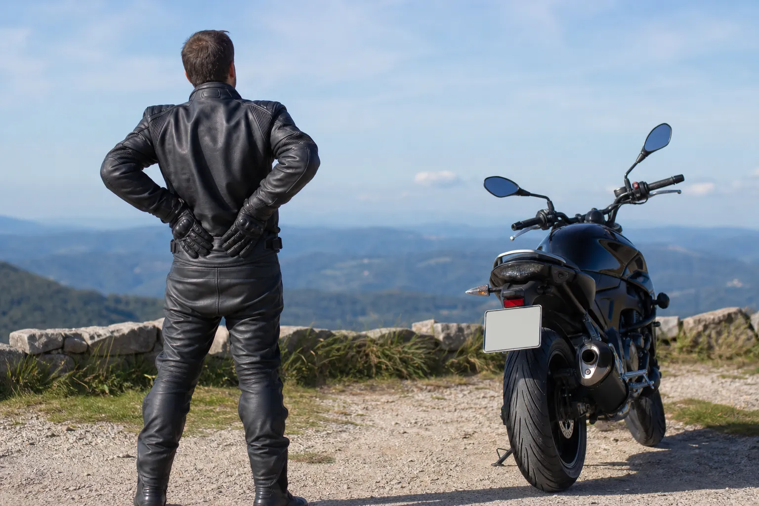 Motard en tenue de cuir noir, moto noire sur route de montagne.