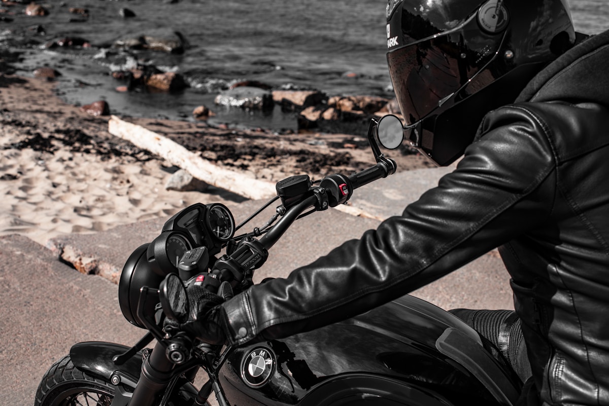 Motard en équipement de sécurité sur une moto noire près de la mer.