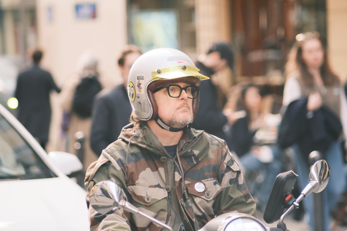 Homme en tenue de camouflage et casque de moto dans une foule urbaine.