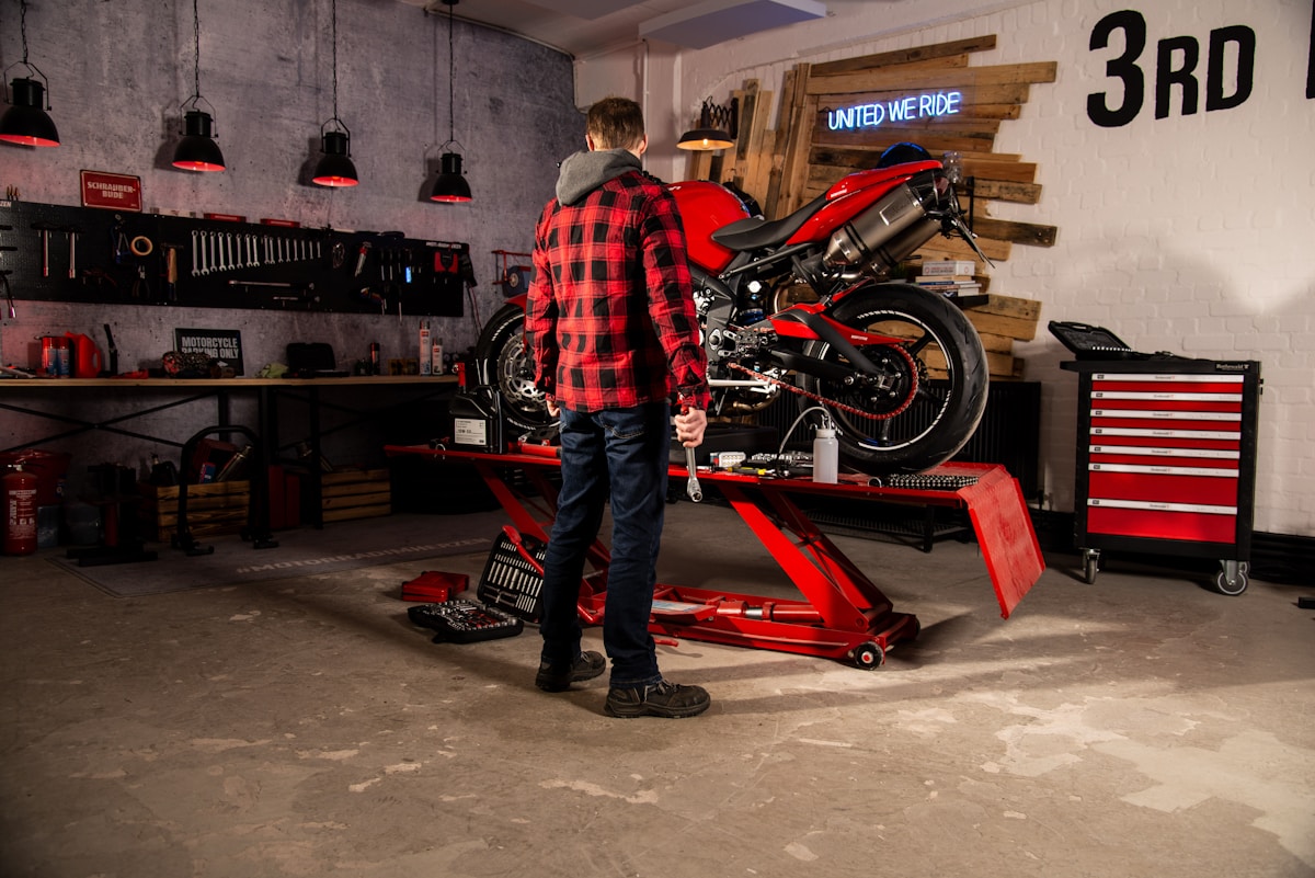 Atelier de réparation de moto avec un homme en chemise à carreaux travaillant sur une moto rouge.