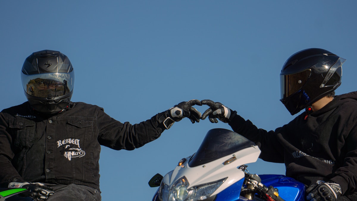Deux motards en équipement de sécurité se saluent sur une moto bleue.