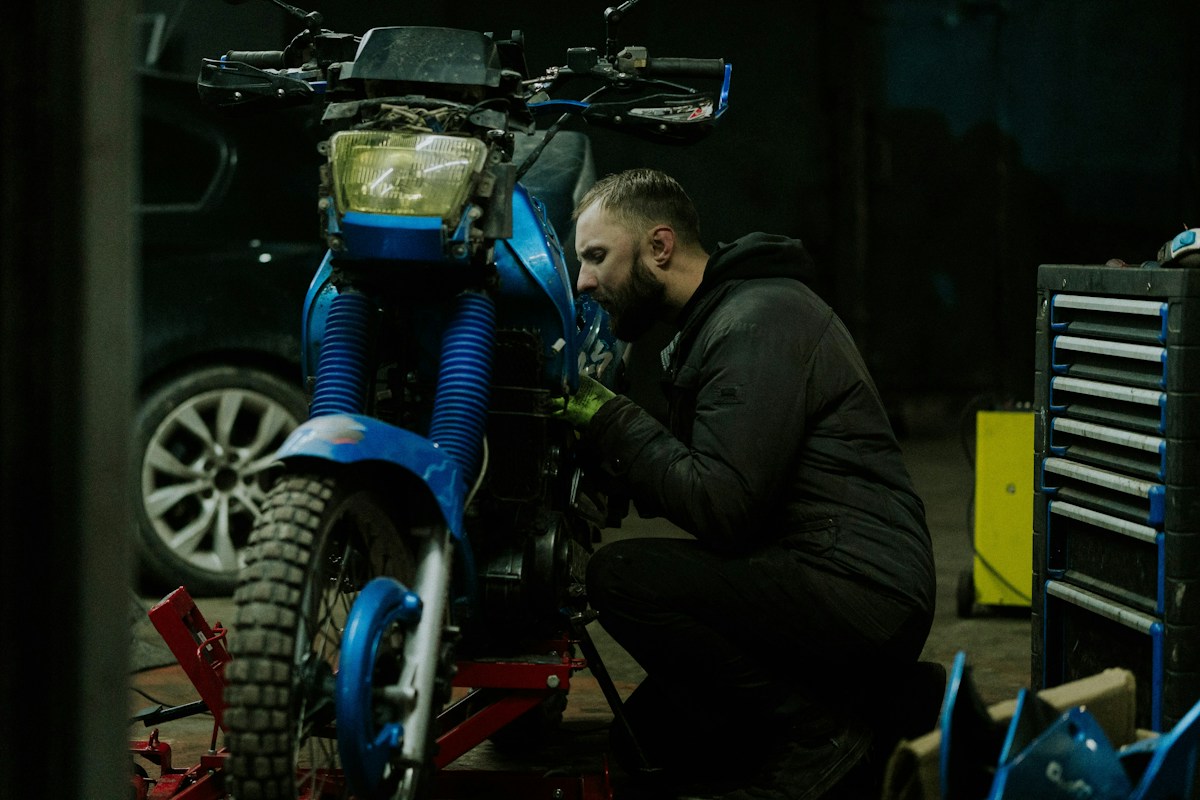 Mécanicien réparant une moto tout-terrain bleue dans un atelier sombre