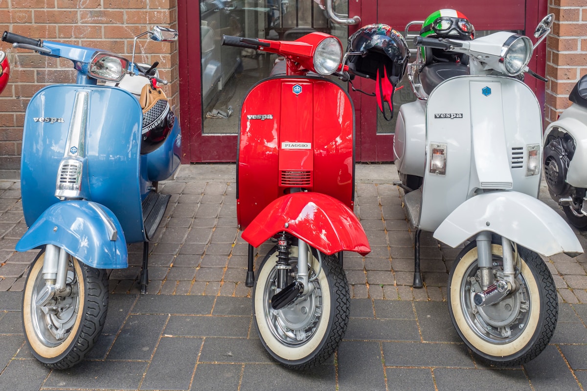 Scooters Vespa rouges, bleus et blancs alignés devant un mur de briques.