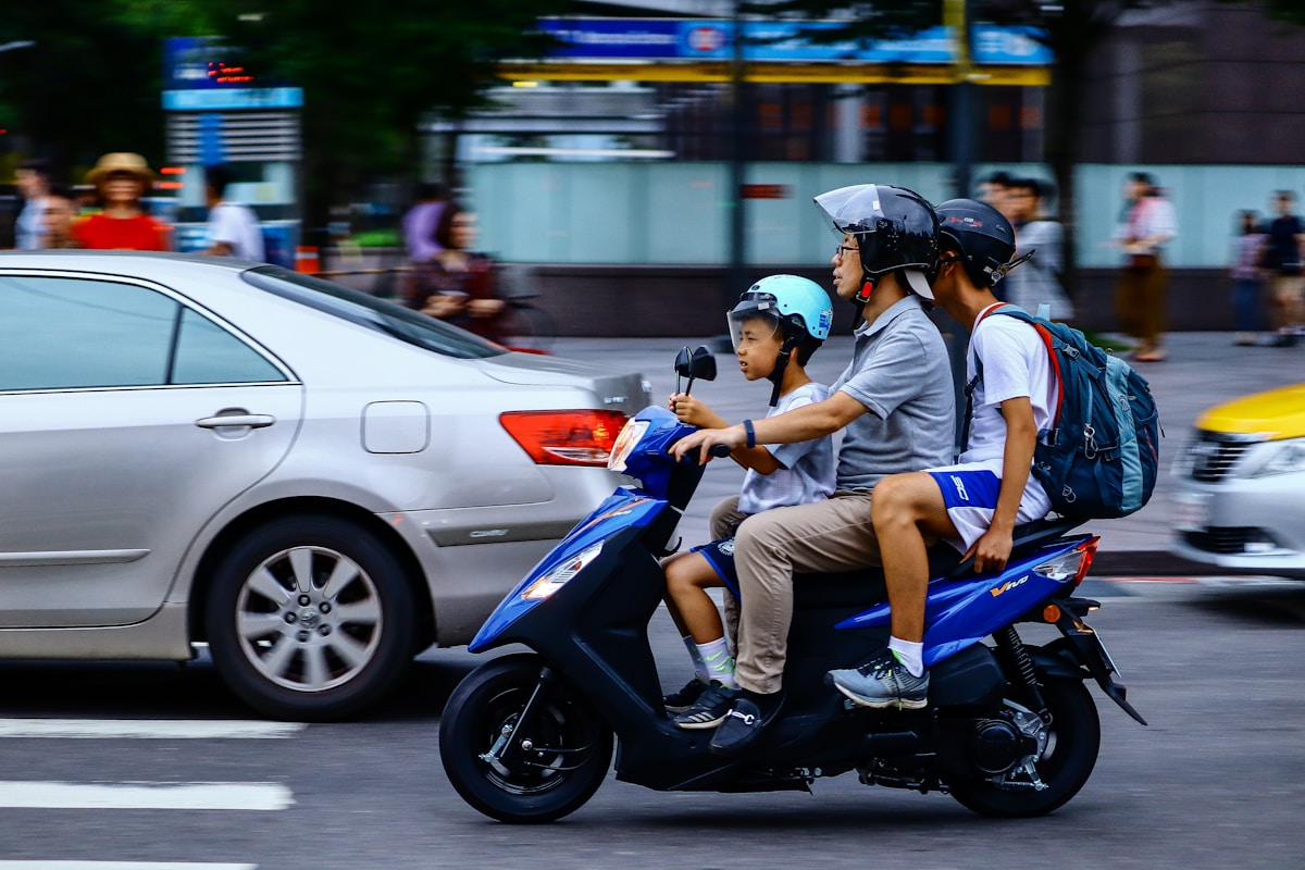 Famille sur un scooter bleu traversant une rue animée.