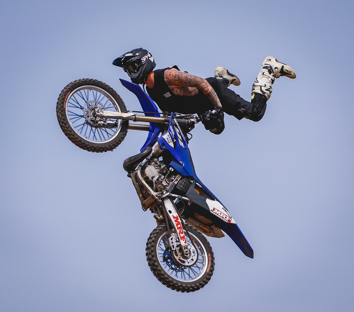 Motocycliste effectuant un saut acrobatique sur une moto de motocross bleue.