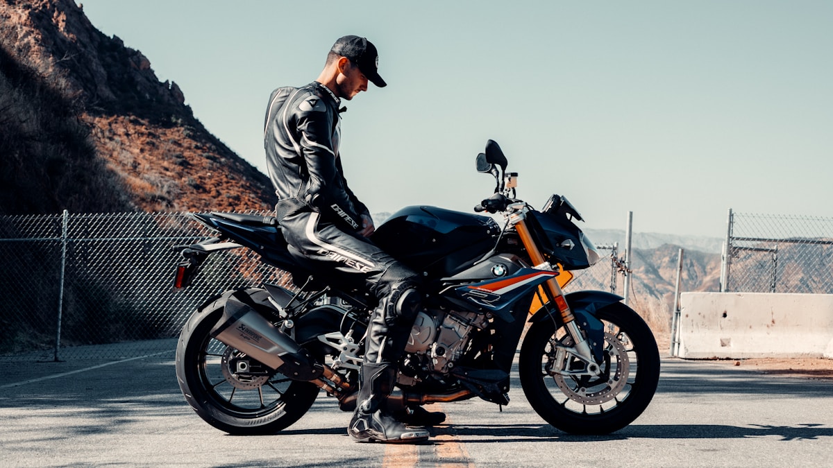 Homme sur une moto de sport noire et orange dans un paysage montagneux.