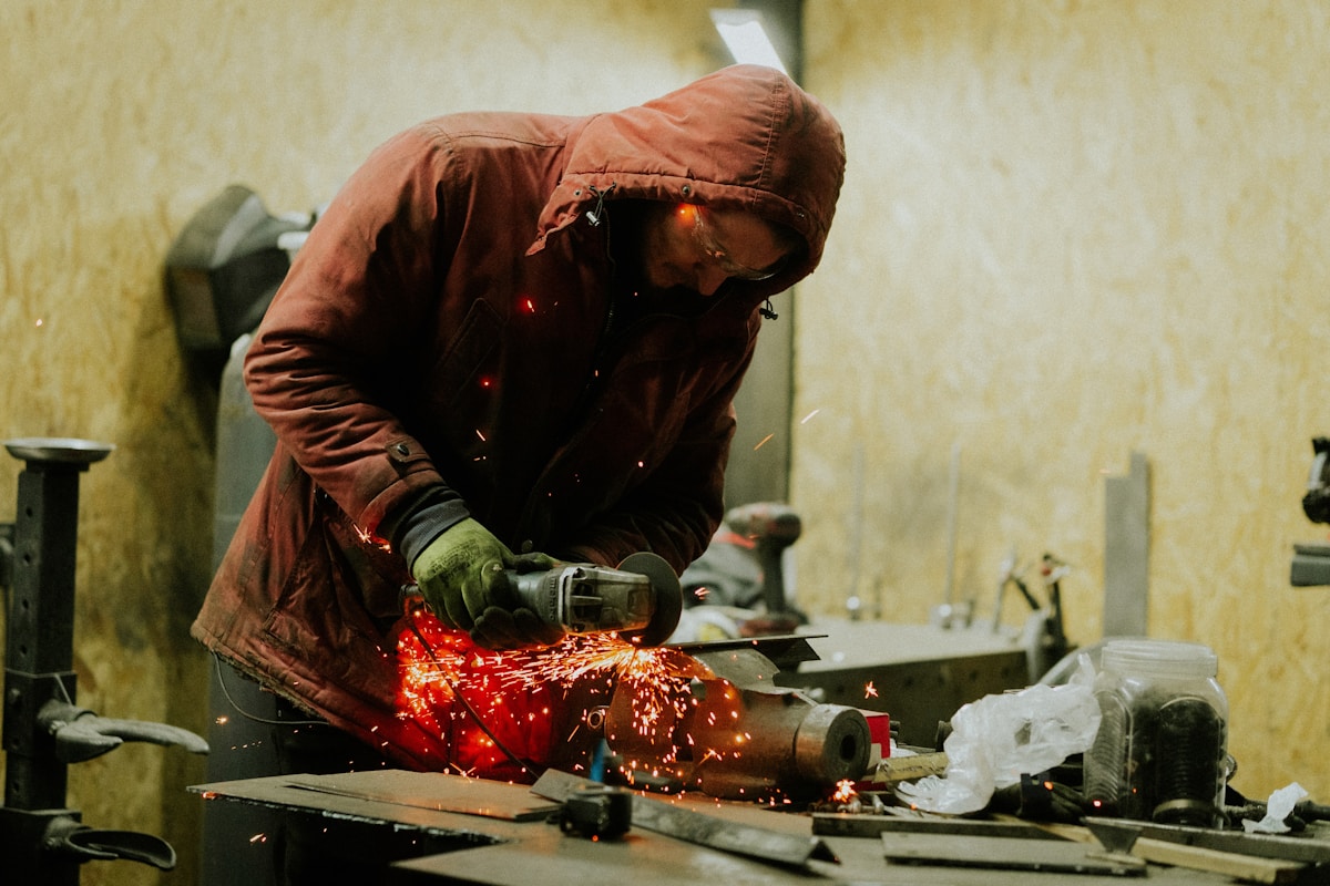 Homme en veste de travail utilisant une meuleuse électrique dans un atelier.